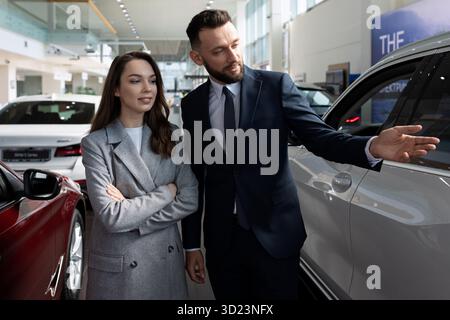 Représentant d'une concession automobile présentant une voiture neuve à une jeune femme acheteuse Banque D'Images