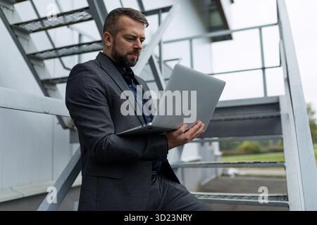 Homme d'affaires travaillant sur ordinateur portable en ligne à l'extérieur Banque D'Images