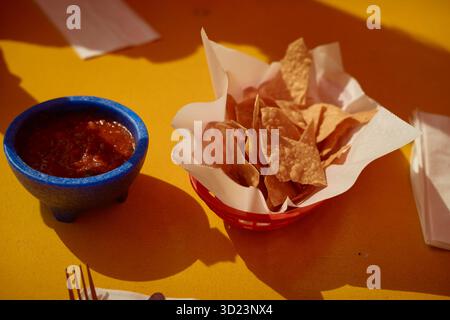 Chips tortilla croustillantes dans un panier avec un bol de salsa sur une table jaune. Californie, États-Unis Banque D'Images