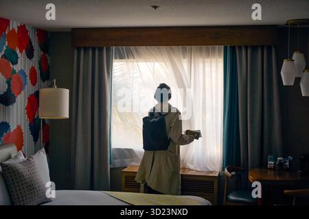 Femme avec sac à dos se tient par la fenêtre de l'hôtel dans une chambre d'hôtel élégante avec un décor mural vibrant. Californie, États-Unis Banque D'Images