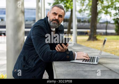 Homme barbu adulte travaillant sur un ordinateur portable à l'extérieur Banque D'Images