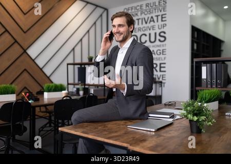 Homme en costume d'affaires parlant au téléphone dans le bureau assis sur la table Banque D'Images