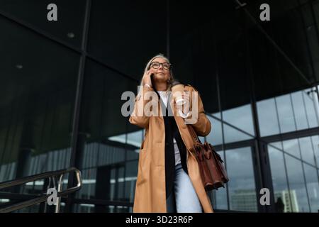 Femme âgée femme d'affaires quittant le bureau parlant sur un téléphone portable Banque D'Images
