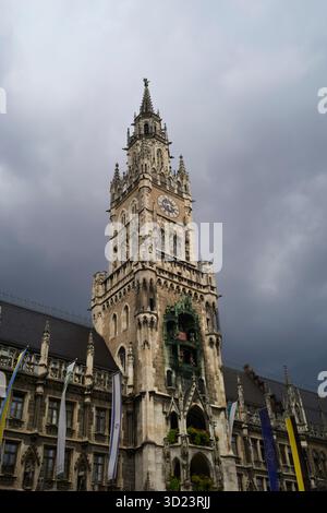 Tour de l'horloge de style gothique sous un ciel nuageux spectaculaire avec des drapeaux ornant le bâtiment. Munich, Allemagne Banque D'Images