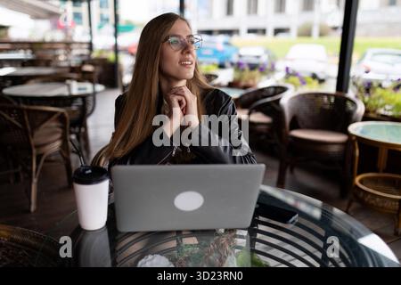 Jeune femme freelance travaillant sur un ordinateur portable dans un café de la ville Banque D'Images