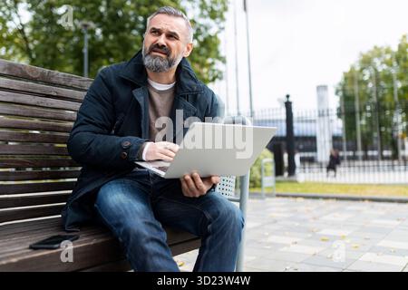 Homme mûr aux cheveux gris avec ordinateur portable à l'extérieur Banque D'Images