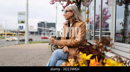 Femme forte de cinquante ans buvant du café tout en étant assise dans la ville Banque D'Images