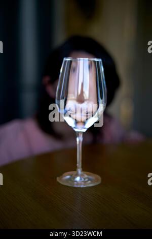 Verre à vin rempli d'eau créant un reflet déformé d'une personne en arrière-plan. Banque D'Images