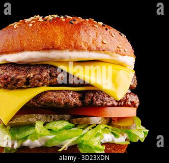 Un hamburger appétissant se compose de deux viandes de bœuf juteuses recouvertes de fromage cheddar, de laitue fraîche, de tomates tranchées, de cornichons et de sauce crémeuse, tout dans Banque D'Images