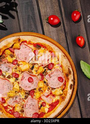 Délicieuse pizza garnie de jambon, de viande de poulet et de tomates cerises sur une table en bois Banque D'Images