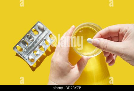 Mains tenant une pilule et un verre d'eau avec blister vide sur Bright Banque D'Images
