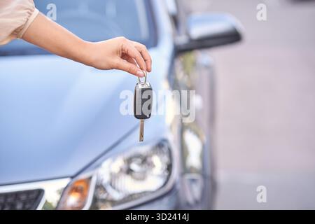 Main féminine tenant la clé de voiture près du véhicule argenté dans un cadre extérieur Banque D'Images
