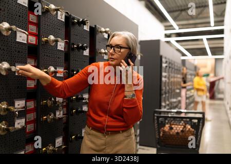 Femme magasinant pour des matériaux d'amélioration de la maison tout en parlant sur son téléphone dans une allée de magasin de détail Banque D'Images