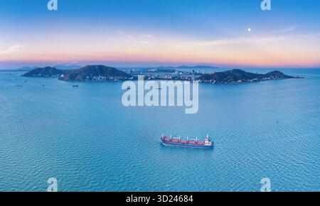 Vue aérienne d'un cargo naviguant sur la mer tranquille vers les îles lointaines sous le ciel crépusculaire de couleur pastel, Vung Tau, Vietnam. Banque D'Images