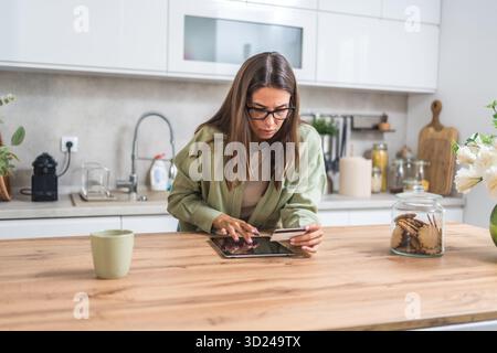 Jeune femme anxieuse décidant de payer ou non en ligne, tenant une carte de crédit et regardant une tablette préoccupée par la fraude, les frais cachés et le budget serré Banque D'Images