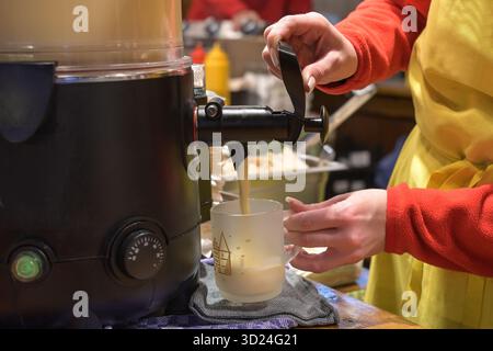 Mains d'une jeune femme versant du lait de poule chaud d'une cuisinière dans une tasse en verre sur le marché de Noël, boisson chaude traditionnelle avec de l'alcool pendant les vacances d'hiver Banque D'Images