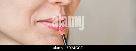 Femme caucasienne appliquant le rouge à lèvres rose gros plan avec le pinceau brillant à lèvres Banque D'Images
