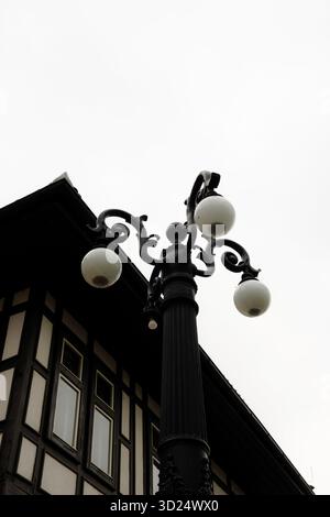 Vue rapprochée d'un lampadaire vintage orné avec des globes de verre ronds contre un ciel couvert, à côté d'un bâtiment traditionnel de style européen Banque D'Images