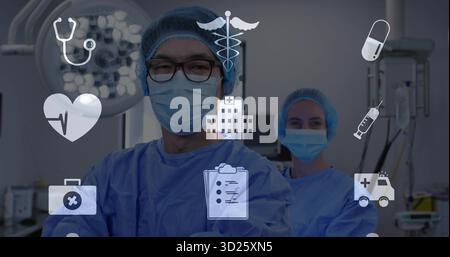 Chirurgien masculin croisant les bras dans des gommages bleus en salle d'opération, avec des plafonniers et des icônes médicales Banque D'Images