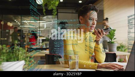 Dactylographier femme dans un pull jaune parlant dans un smartphone au bureau avec un code sur la cloison en verre Banque D'Images