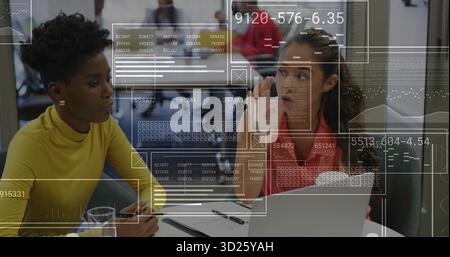 Deux femmes en tenue d'affaires faisant des gestes à l'ordinateur portable et examinant les documents de carte dans le bureau Banque D'Images