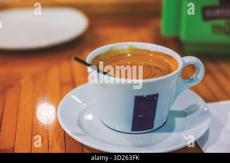 Vue rapprochée de l'espresso chaud avec une crème épaisse dans une tasse en céramique blanche sur soucoupe placée sur le comptoir en bois dans le café. Miami. ÉTATS-UNIS. Banque D'Images