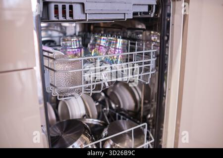 Vaisselle, verres et casseroles sont soigneusement disposés dans un lave-vaisselle propre et moderne dans une cuisine bien éclairée. Banque D'Images