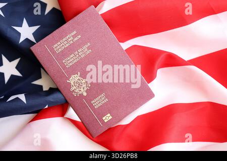 Passeport belge sur grand drapeau agitant des États-Unis d'Amérique close up. Visa AMÉRICAIN et concept d'immigration Banque D'Images