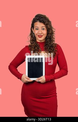 Femme en robe rouge tenant une tablette verticalement avec un écran noir vierge Banque D'Images