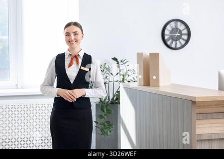 Heureux réceptionniste en uniforme près de la réception à l'intérieur Banque D'Images