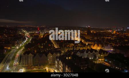 La vue aérienne nocturne de Gdansk, en Pologne, montre les lumières de la vieille ville, l'église St Marys, la flèche de l'hôtel de ville principal, les fronts de la rivière Motlawa, la grue de Gdansk et la circulation Banque D'Images