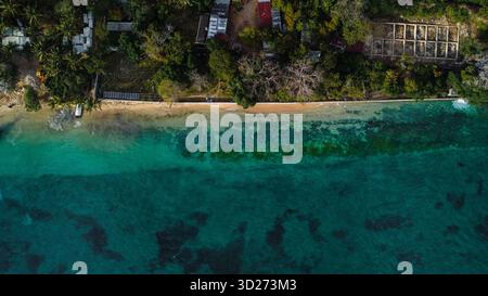 Étroite étendue de plage de sable où la terre luxuriante et verdoyante rencontre les eaux claires, turquoise et bleu profond de l'océan. Banque D'Images