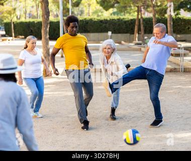 Joyeux amis multinationaux jouant au football sur un terrain de jeu sablonneux lors d'une chaude soirée de printemps Banque D'Images