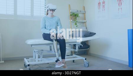Femme de formation portant des leggings en utilisant un casque VR sur la table de thérapie à la clinique avec un membre prothétique Banque D'Images