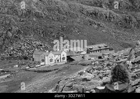 Le Pen y Pass Warden Centre, niché dans le paysage spectaculaire de Nant Gwynant, offre une base vitale pour les aventuriers qui s'attaquent à la formidable chaîne de Snowdon. Ce bâtiment historique, construit en pierre grise, offre des installations essentielles pour les grimpeurs et les marcheurs, stratégiquement positionné près du pied du col Pen y, la route la plus populaire jusqu'à Snowdon. Son emplacement surélevé offre une vue panoramique imprenable sur les sommets et les vallées des montagnes environnantes, un témoignage de la beauté accidentée de la région et du terrain difficile. Banque D'Images