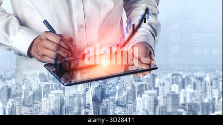 Une personne écrit sur une tablette numérique affichant un graphique de croissance dynamique, symbolisant l'avancement de l'entreprise dans un paysage urbain. Imputer Banque D'Images
