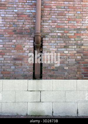 Gros plan vertical d'un détail architectural urbain avec un mur de briques altérées avec une descente marron-rouge proéminente qui descend au centre Banque D'Images