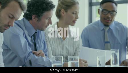 Quatre professionnels examinant des documents imprimés et prenant des notes dans une salle de conférence moderne, verres à eau Banque D'Images