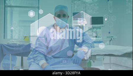 Chirurgien masculin assis portant des gommages bleus avec masque et gants dans une salle chirurgicale avec moniteurs Banque D'Images