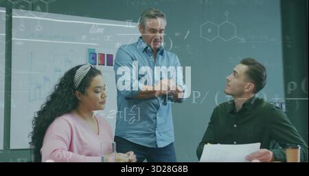 Homme mature gestuel en chemise bleu clair présentant dans la salle de conférence, avec des diagrammes de tableau blanc Banque D'Images