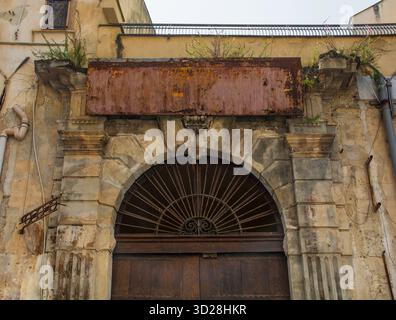 Entrée dans un ancien hôtel dans le quartier de Kalsa, Palerme, Sicile, Italie. Une arche de blocs de pierre fortement altérés. Au-dessus de la porte, un panneau en métal rouillé Banque D'Images