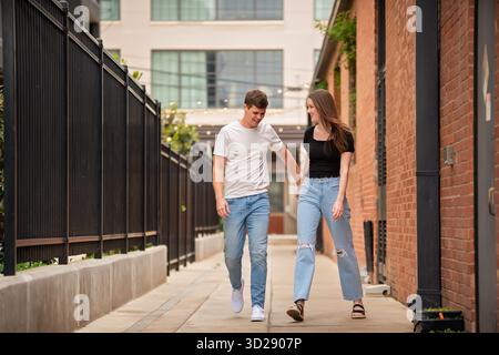 Un couple riant marche main dans la main dans la ruelle urbaine Banque D'Images