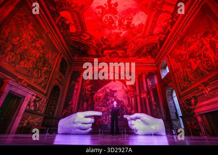 Londres, Royaume-Uni. 31 octobre 2025. Personnel avec les installations de Peter Walker 'Connection' and Identity' dans le Painted Hall de l'Old Royal Naval College, Greenwich. « Identity » montre huit colonnes suspendues illuminées, évoquant les structures de l'ADN, et « Connection » est une réinterprétation moderne de la création d'Adam de Michel-Ange, remplaçant les mains traditionnellement masculines par des moulages de mains féminines. Crédit : Imageplotter/Alamy Live News Banque D'Images