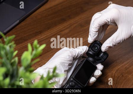 Poznan, Pologne - 16 octobre 2025 : vue de dessus de la caméra DJI Osmo Pocket sur un bureau en bois, manipulée avec précision par les mains dans des gants blancs pour filmi Banque D'Images