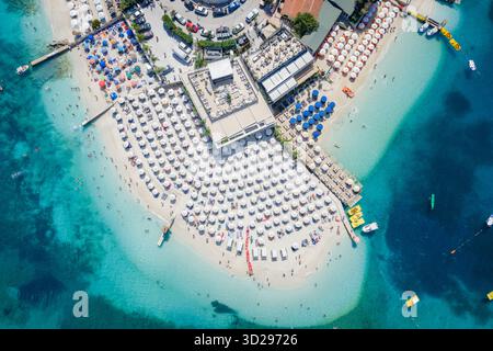 Vue aérienne de la plage animée et ensoleillée de Ksamil, où les eaux turquoises rencontrent le sable blanc parsemé de parasols et de bateaux, Ksamil, Vlor, Alb Banque D'Images