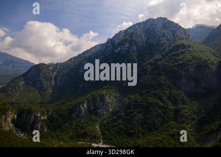 Vue aérienne des montagnes escarpées recouvertes de forêts verdoyantes, montez vers un ciel parsemé de nuages blancs et moelleux, créant un contraste fascinant de te Banque D'Images