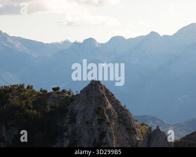 Vue aérienne d'un pic déchiqueté, touché par la lumière du soleil, perçant le ciel, avec des figures silhouettées contre l'horizon à Teth, comté de Shkodër, Albanie. Banque D'Images