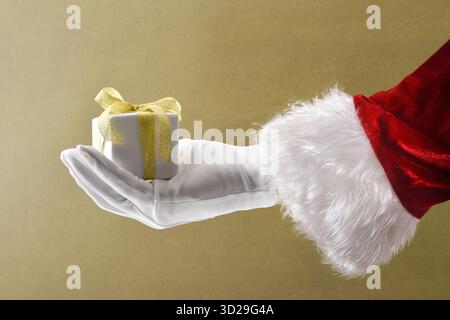 Paquet cadeau main de Père Noël en costume et gants avec papier blanc et noeud doré sur fond isolé brun. Banque D'Images