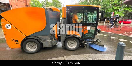 Berlin, Allemagne - 05 juin 2025 : la machine de nettoyage de rue nettoie activement les rues urbaines avec le cycliste qui passe. Banque D'Images