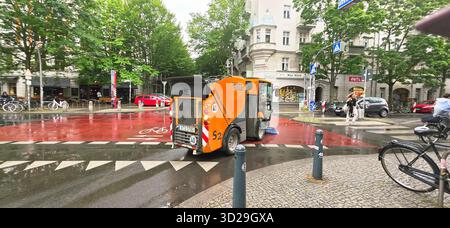 Berlin, Allemagne - 05 juin 2025 : le véhicule de nettoyage des rues Orange est garé dans une rue urbaine entourée d'arbres et de bâtiments. Banque D'Images